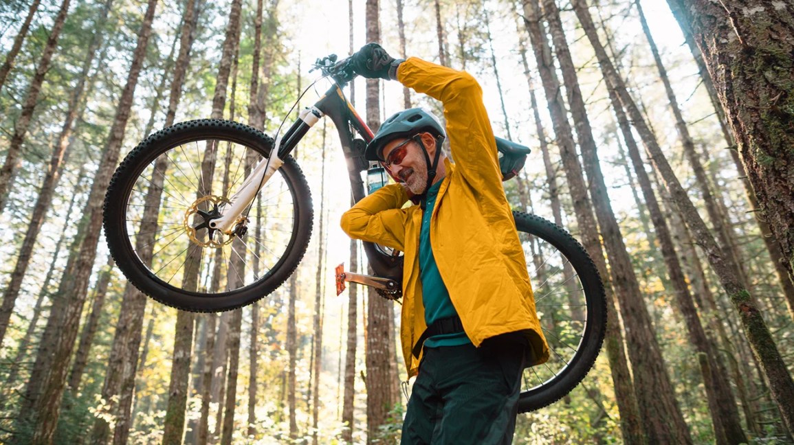Person holding their bike in the air as they hike through scenic woods.