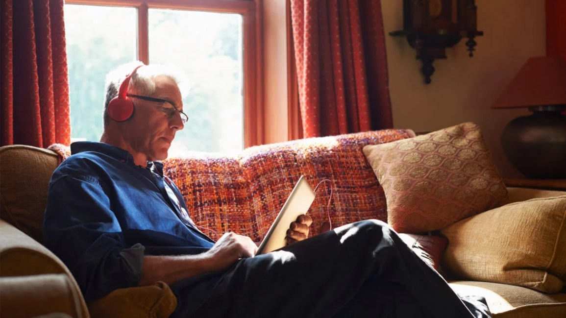 A person with glasses sitting on a nice couch and reading on an iPad
